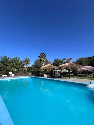 a blue swimming pool with straw umbrellas and chairs at Hotel y Cabañas Capri in Villa Carlos Paz