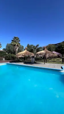 a swimming pool with straw umbrellas and a pool at Hotel y Cabañas Capri in Villa Carlos Paz