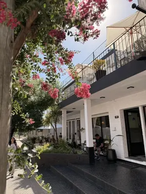a person sitting on a bench in front of a building with pink flowers at Hotel Centro SJ in Villa Carlos Paz