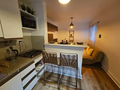 a small kitchen with two bar stools and a bed at Departamento en B Gral Paz, a metros de Hospital Italiano in Cordoba