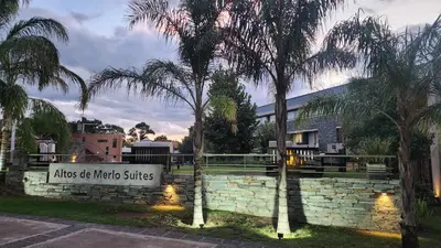 a sign in front of a stone wall with palm trees at Altos De Merlo Suites in Merlo