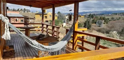 a hammock on a deck with a view of a house at Cabaña Don Mario in Villa Yacanto