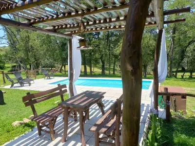 a picnic table and chairs under a pergola next to a pool at Cabaña La Maruca Calamuchita Sierras de Córdoba in San Clemente