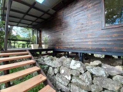 a wooden building with a stone wall and benches at Cabaña La Maruca Calamuchita Sierras de Córdoba in San Clemente