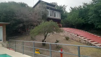 a house with a tree in front of a building at Complejo de cabañas el Winon in Cuesta Blanca