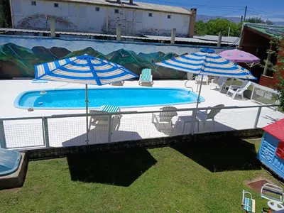 a swimming pool with two umbrellas and chairs next to it at Cabañas LAS AMELIAS in Villa Cura Brochero