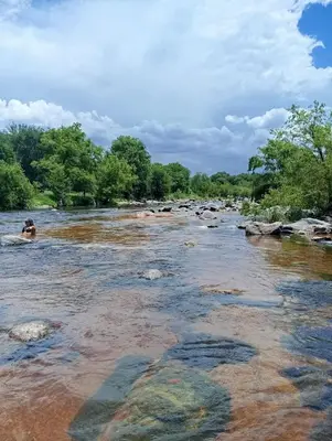 a river with rocks and a person swimming in it at Duplex Único Frente al Río in Villa Carlos Paz