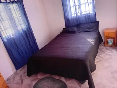 a bedroom with a bed with blue curtains and a window at La Gringa in Villa Parque Siquiman