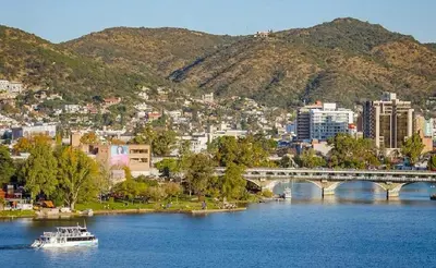 a boat on a river with a bridge and a city at La Pequeña Villa in Villa Carlos Paz