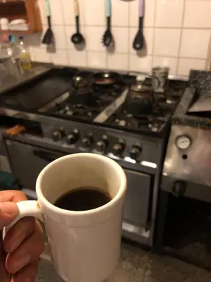 a person holding a cup of coffee in front of a stove at Casa Kuku in Las Rabonas