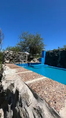a swimming pool with a stone wall and blue water at Cabaña hasta siete personas Complejo Aires de montaña siquiman in Villa Parque Siquiman
