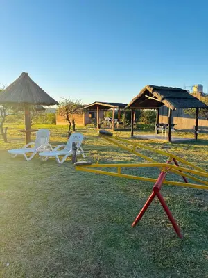 a group of chairs and an umbrella in a field at Complejo de cabañas El Nido in Mina Clavero