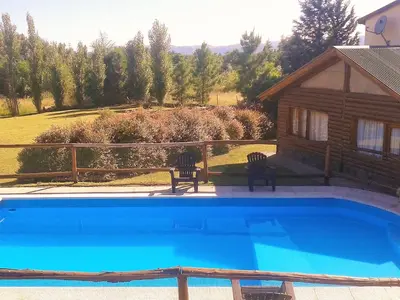 a swimming pool with two chairs and a cabin at Ensueño Cabañas in Los Reartes