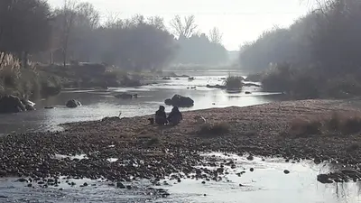 two people sitting on the shore of a river at Ensueño Cabañas in Los Reartes