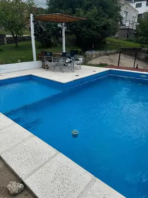 a blue swimming pool with a table and an umbrella at Vistas del Valle II in Villa Carlos Paz