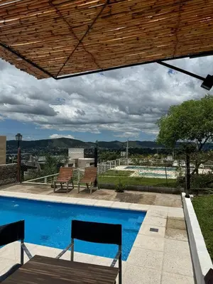 a swimming pool with two chairs and a wooden roof at Vistas del Valle II in Villa Carlos Paz