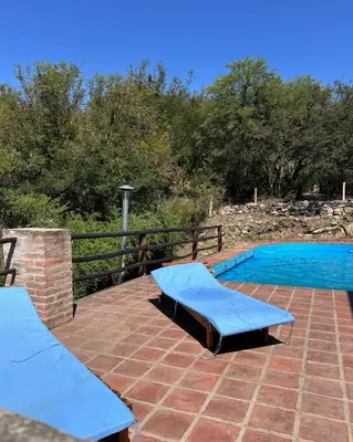 a swimming pool with two blue benches on a brick patio at Mirador De Las Sierras in Villa Serranita