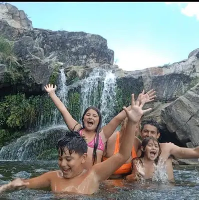 a group of children in the water in front of a waterfall at las huertitas de milele in La Porteña
