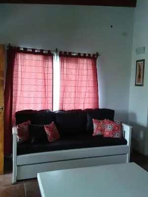 a black couch in front of a window with red curtains at Complejo Los Cuatro Elfos in La Estancia