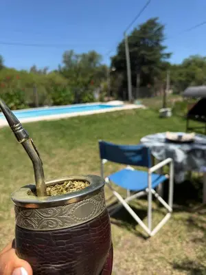 a person holding a drink in a cup next to a chair at El Algarrobo in Villa del Dique