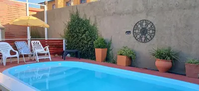 a swimming pool with chairs and a table and an umbrella at Departamentos Ecuador in Villa Carlos Paz