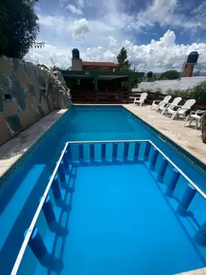 a blue swimming pool with chairs and a house at Casa Familiar Centrica Abdulle in Villa Cura Brochero