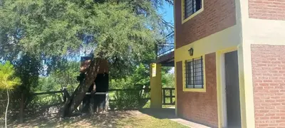 a tree next to a building with a fence at Cabaña los algarrobos in Mina Clavero
