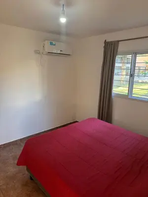 a red bed in a white room with a window at Cabañas con pileta y aire acondicionado empalme in Villa Carlos Paz