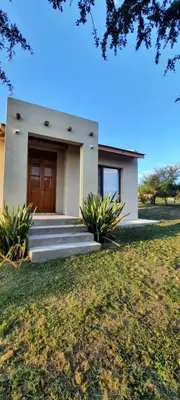 a house with a wooden door and a grass field at Casa de Campo Roca - Exclusivo para Parejas in Villa Cura Brochero