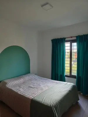 a bedroom with a bed with green curtains and a window at Casa de campo Los Gurises in Alta Gracia