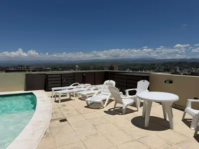 a patio with white chairs and tables and a pool at Torre Melos Carlos Paz in Villa Carlos Paz
