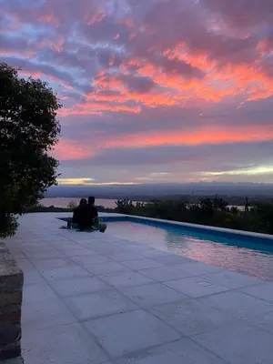 two people sitting next to a swimming pool at sunset at Complejo DOS LUNAS in La Porteña