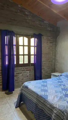 a bedroom with a bed with blue curtains and a window at Cabaña piedraPintada in San Javier