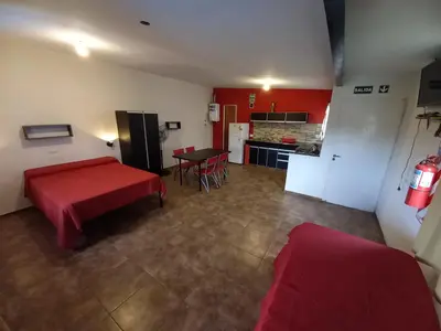 a living room with a red table and a kitchen at Monoambiente los ceibos in Villa Santa Cruz del Lago