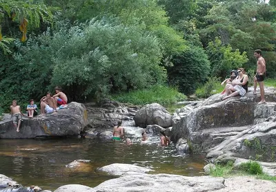 a group of people sitting on rocks in a river at Descanso en Tanti - Turismo y Bienestar in Tanti