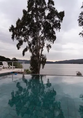 a tree sitting next to a swimming pool next to a lake at Complejo Palo Blanco in Villa Carlos Paz