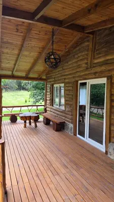 a porch of a wooden cabin with benches and a chandelier at Paraiso en el Manantial in Villa General Belgrano