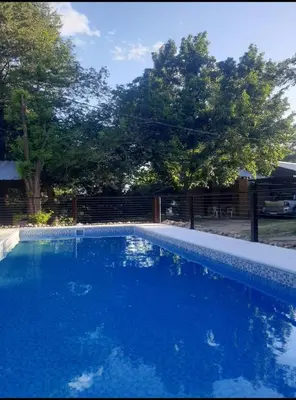a blue swimming pool with a fence and trees at Colores de Traslasierra in Mina Clavero
