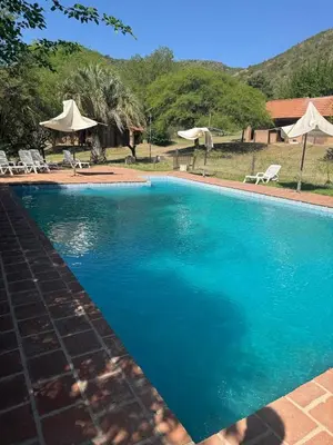 a large blue swimming pool with chairs and umbrellas at Hostel Planeta Terminal VGB in Villa General Belgrano