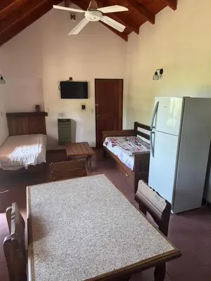 a living room with two beds and a refrigerator at Hostel Planeta Terminal VGB in Villa General Belgrano