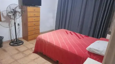 a bedroom with a red bed and a dresser with a fan at Habitacion en Casa de Olga in Alta Gracia