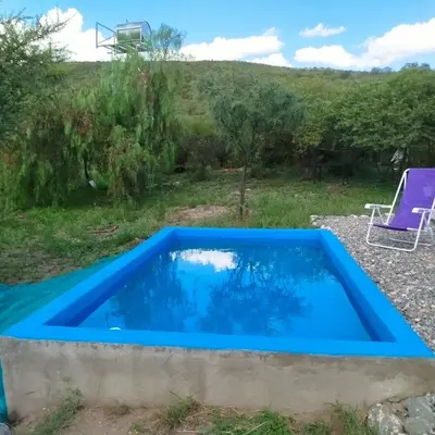 a blue swimming pool in a yard with a chair at Entre Tanto in Luyaba