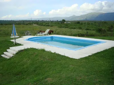 a swimming pool in a field with a chair and an umbrella at Casa de Campo con Pileta - Estancia La Amistad in Villa Santa Cruz del Lago