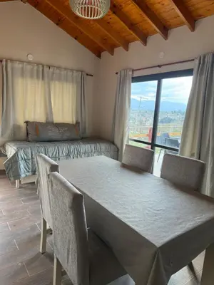 a dining room with a table and a bed and a window at L&M Cabañas Villa Yacanto in Villa Yacanto