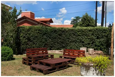 two wooden benches sitting in the grass near a hedge at El Camino Hostel in Mina Clavero