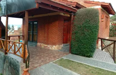 a brick house with a door and a hedge at Cabañas Layken in Villa Carlos Paz