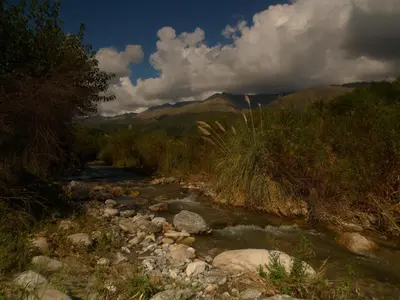 a river with rocks and trees and mountains in the background at Samsara Traslasierra in Los Hornillos