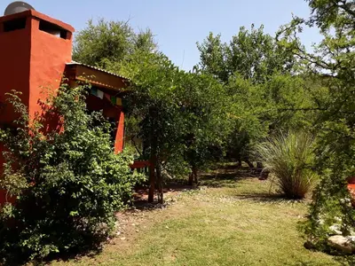 a garden with trees and a red building at Samsara Traslasierra in Los Hornillos