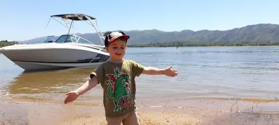 a young boy standing on the beach near a boat at Cañada Al Lago in Villa Parque Siquiman