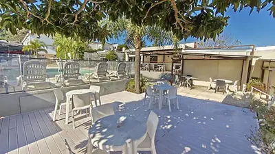 a patio with white chairs and tables and a tree at Hotel Linz in Villa Carlos Paz